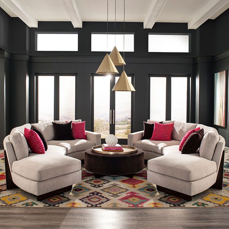 Two curved couches grouped on area rug facing each other with round hassock in center. Backdrop are large glass doors and windows.