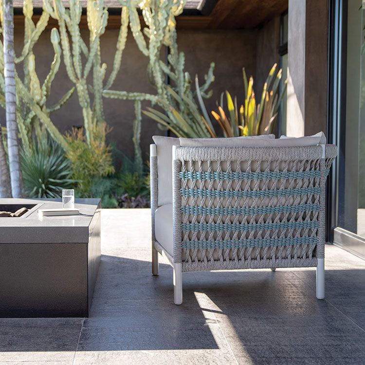 Small rattan chair next to firepit with cactus garden in background.