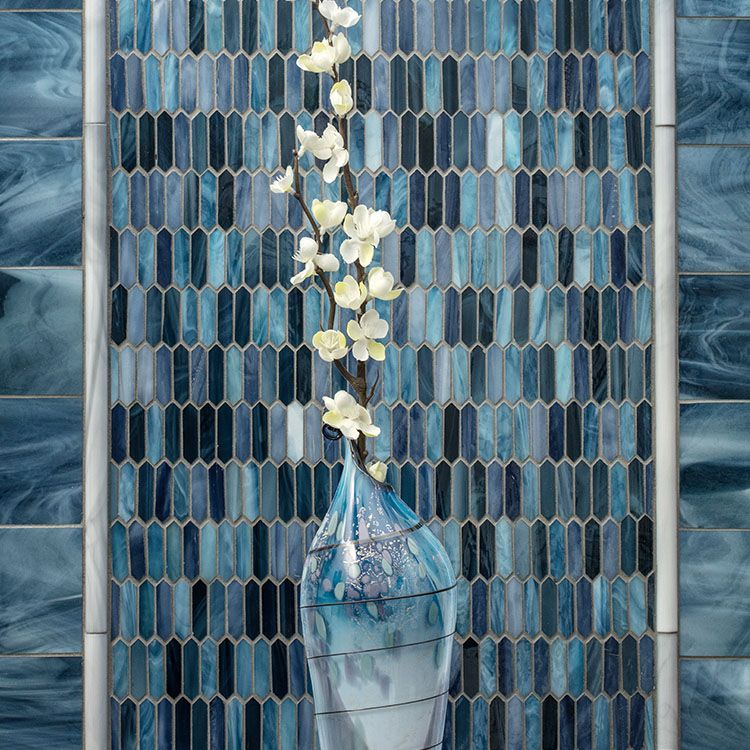 Stained glass wall with two different sections behind a blown glass vase holding apple blossoms.