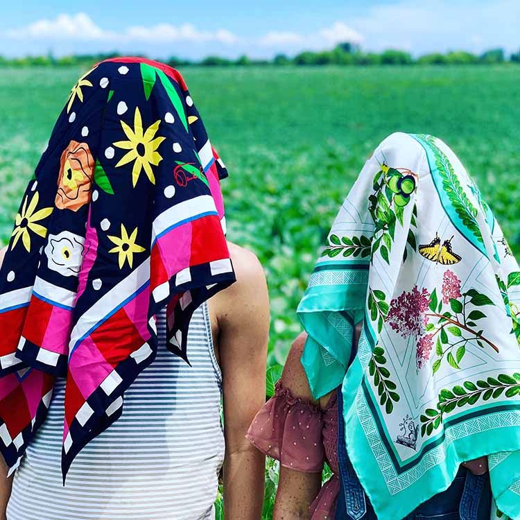 Two people with patterned scarves hiding their heads with a field in background.